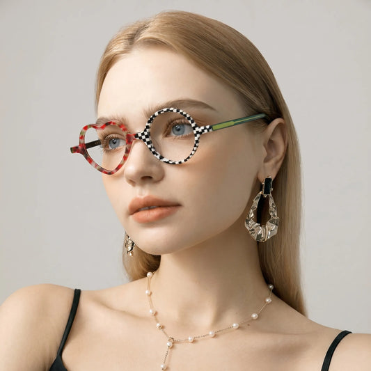 Model showcasing the Checker Red Pop VoyueLens Whimsy Pop frame in a lifestyle setting. Bold red and black asymmetrical frame with heart and round lenses.