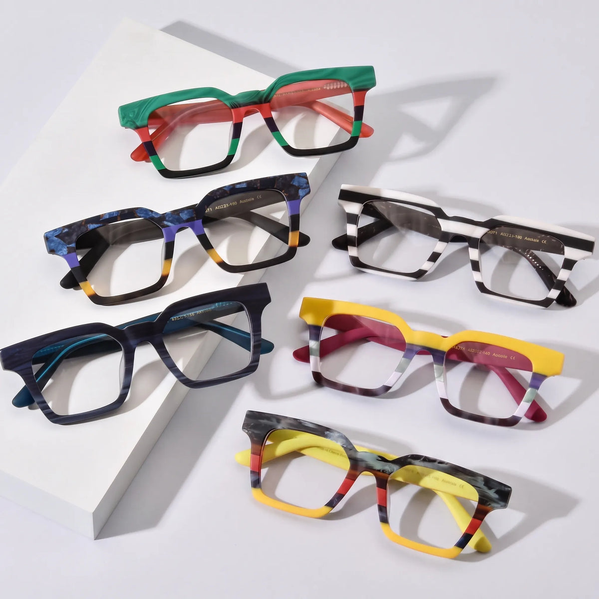 Group display of VoyueLens BlockForm Square Eyeglasses in six color variants including Jungle Stripe, Midnight Fade, Zebra Noir, Indigo Mist, Lemon Sorbet, and Citrus Fade – laid out on pink background in aesthetic top-down view.