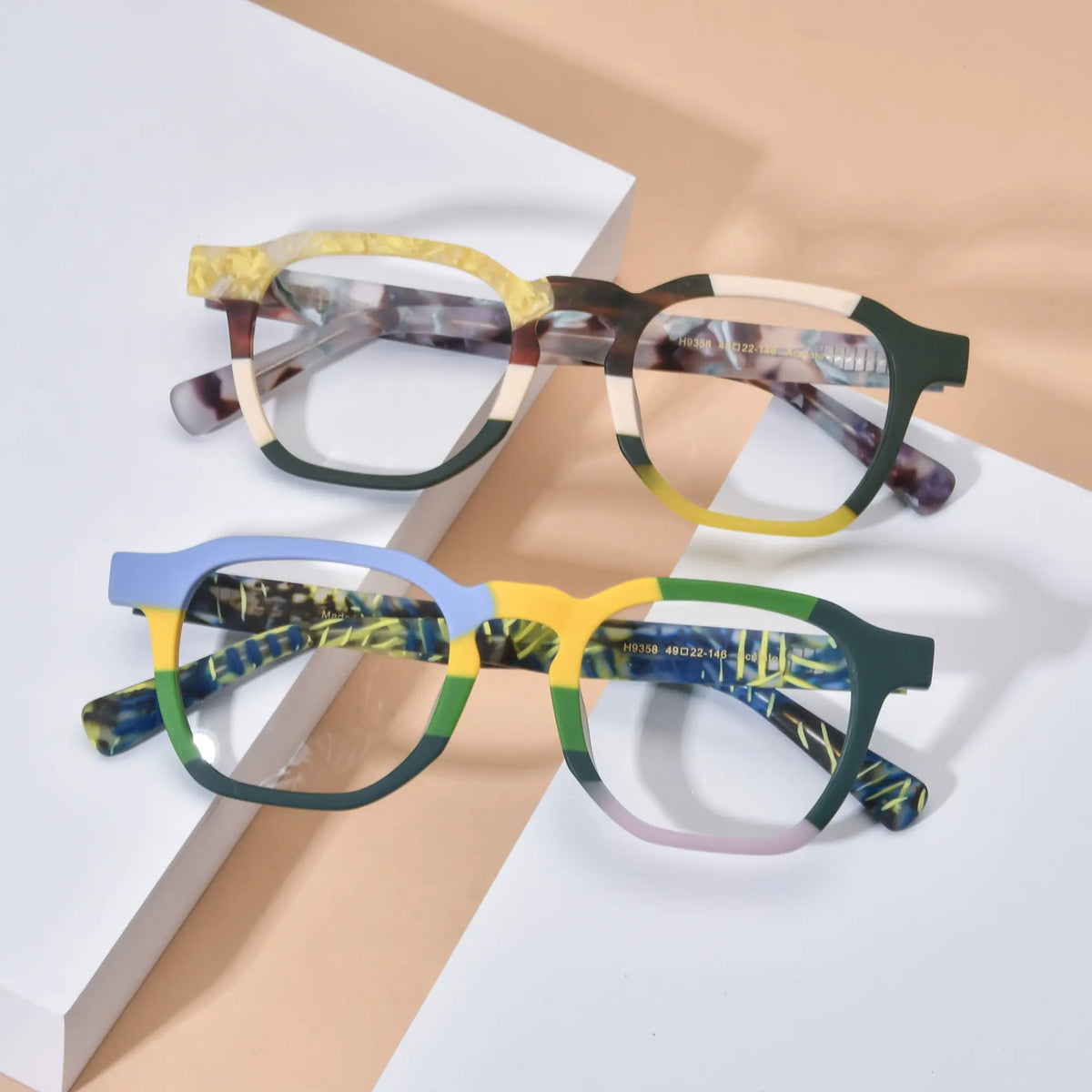 Lifestyle flatlay image showcasing VoyueLens VL19358 colorblock square glasses in both Citrus Fade and Ocean Tortoiseshell variants, styled on a soft neutral background to highlight vibrant frame contrasts and artistic acetate detailing.