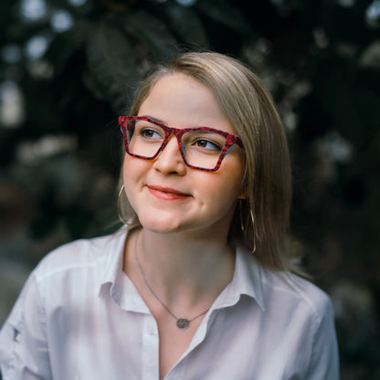 Model wearing VoyueLens Crimson Nebula butterfly frame in matte crimson red with cosmic black accents, demonstrating stylish fit for wide faces.