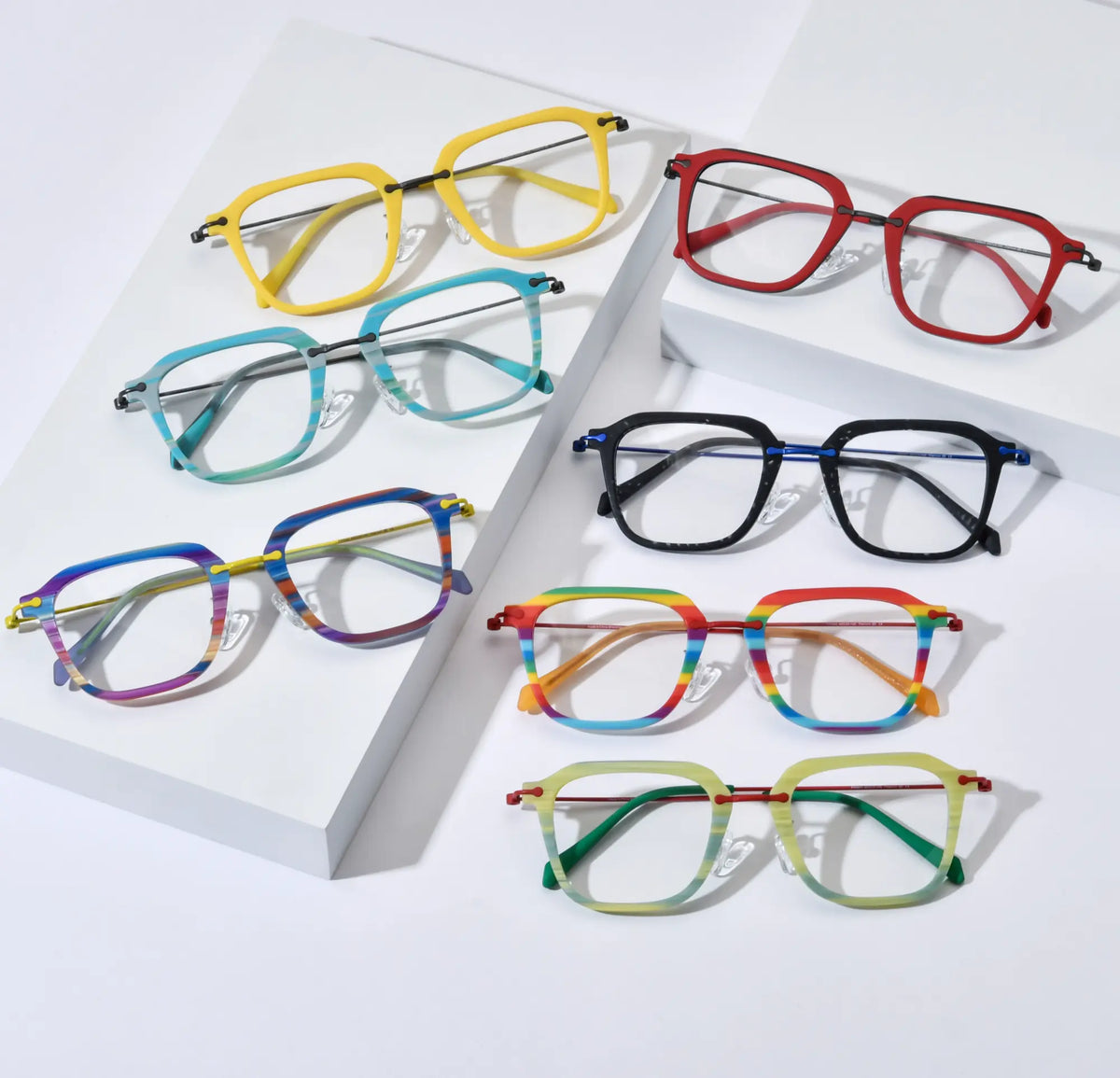 Stylish flat lay composition showcasing the full color range of VoyueLens VL185843 Urban Vision eyeglasses. Includes all seven vibrant variants: Sunshine Yellow, Crimson Alloy, Glacier Teal, Midnight Graphite, Vivid Violet Stripe, Rainbow Parade, and Citrus Mist — arranged aesthetically on staggered white platforms, highlighting the modern square design and titanium detailing.