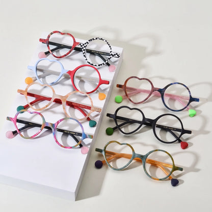 Group display of VoyueLens VL19377 Whimsy Pop Eyeglasses in all seven color variants, featuring asymmetric heart and round lenses on a pink background. Stylish matte acetate frames with vibrant tones including Checker Red Pop, Ice Blue Cherry, Honey Peach, Cocoa Marble, Citrus Jungle, Rainbow Twist, and Charcoal Dusk.